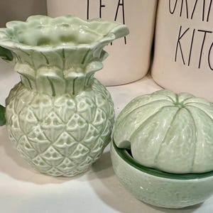 Może przedstawiać: Zielony ceramiczny dzbanek w kształcie ananasa i zielona ceramiczna cukiernica w kształcie limonki z pokrywką.