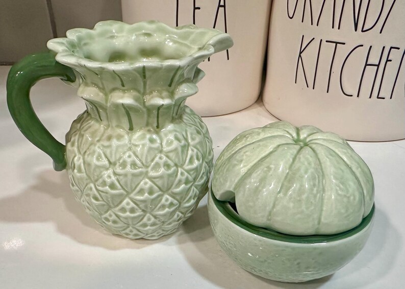 Może przedstawiać: Zielony ceramiczny dzbanek w kształcie ananasa i zielona ceramiczna cukiernica w kształcie limonki z pokrywką.