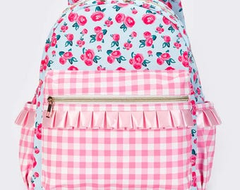 May include: A backpack featuring a light blue base with a pink rose floral pattern. The front pocket displays a pink and white gingham check print with a horizontal pink ruffled trim. It includes gold-tone zippers and side pockets.