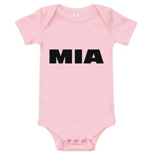 Puede incluir: Un body de bebé rosa claro con el nombre "MIA" impreso en letras negras grandes. El body de manga corta tiene corchetes en la entrepierna. Una prenda sencilla y dulce para un bebé.