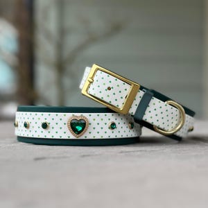 May include: Two dog collars with a white base and green heart pattern. One collar has a gold buckle and the other has a large green heart-shaped rhinestone.