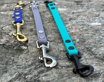 May include: Three dog leash extensions in blue, lavender, and turquoise. The blue strap has gold-tone hardware and rivets. The lavender strap features silver-tone hardware and rivets. The turquoise strap includes black hardware and rivets.