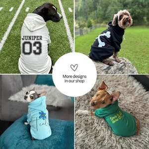May include: A collection of four dog hoodies featuring a white hoodie with the text JUNIPER 03, a black hoodie with a white bone graphic, a light blue hoodie with a blue flower and text, and a green hoodie with the text She's a Meaw One.