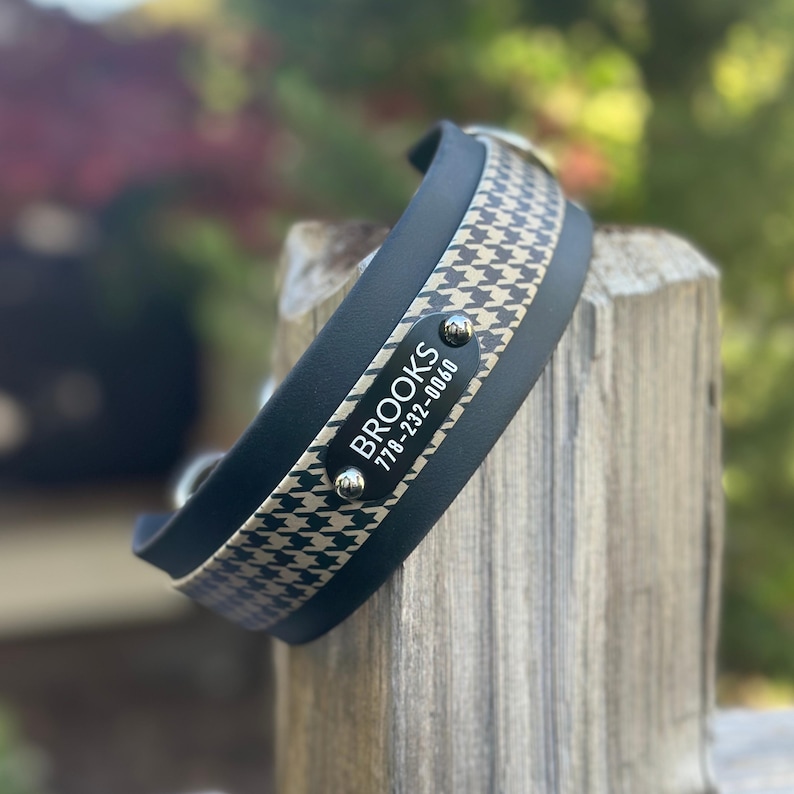 Puede incluir: Un collar para mascota de color azul oscuro con un patr&oacute;n de pata de gallo en beige y azul oscuro. Una placa de identificaci&oacute;n rectangular negra est&aacute; sujeta con dos remaches plateados, mostrando el texto blanco BROOKS y 778-232-0060.