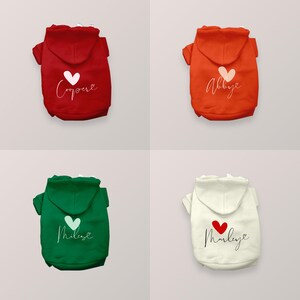 May include: Four pet hoodies in red, orange, green, and cream. Each hoodie features a hood, short sleeves, and a printed design on the back consisting of a heart icon above a name written in cursive script: Cooper, Abbye, Miles, and Marley.
