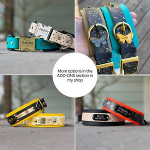 May include: A collection of dog collars in various colors including teal, yellow, black, and orange, featuring metal buckles and nameplates engraved with names and phone numbers. Some collars have patterns like hearts, celestial motifs, or floral prints.