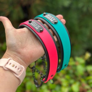 Puede incluir: Dos collares para perro con base negra y capas exteriores en rosa brillante y turquesa. Cada collar tiene una placa de identificaci&oacute;n de metal negro remachada, con los nombres ELLIE y MILEY y el n&uacute;mero 619-213-3682 grabados en blanco.