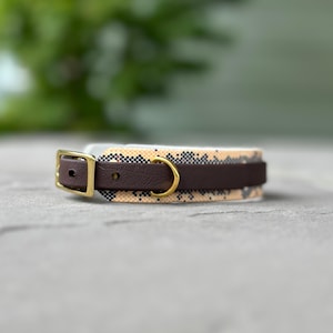 Peut inclure: Un collier pour animaux de compagnie marron et beige avec une boucle et un anneau dorés. Le collier a une sangle en cuir marron foncé et un motif en beige et noir. La boucle est carrée et l'anneau est circulaire.