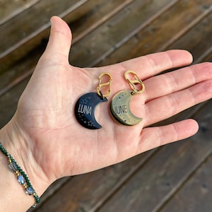 Puede incluir: Dos llaveros de color dorado en forma de media luna con acabado negro y dorado. El llavero de la izquierda tiene el nombre "LUNA" grabado en &eacute;l, y el llavero de la derecha tiene el nombre "JUNE" grabado en &eacute;l.