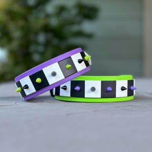Könnte beinhalten: Zwei Schachbrettmuster-Halsbänder mit schwarzen, weißen und grünen Akzenten. Die Halsbänder haben silberne Nieten und schwarze Spikes.