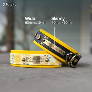 May include: Two pet collars with metal ID tags. One is yellow with a floral pattern and a tag reading ED CINDY YUREK 702 496-4833 702 334-5555. The other is black with a moon phase pattern and a tag reading GRIMM 313-686-5555. Sizes are 60mm x 19mm and 60mm x 10mm.