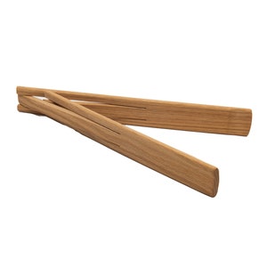 May include: Wooden serving tongs made of light brown wood. The tongs are open, displaying their design. The ends are rounded and the wood grain is visible. The tongs are designed for serving food.