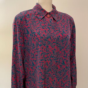 May include: A long-sleeved blouse with a vibrant pattern of teal and burgundy swirls. The blouse features a collared neckline with a single button closure. The fabric appears to be lightweight and flowing.