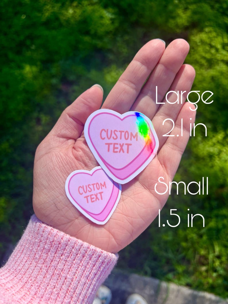 May include: Two pink heart-shaped stickers with a holographic finish. The larger sticker is 2 inches and the smaller sticker is 1.5 inches. Both stickers say "CUSTOM TEXT" in white.
