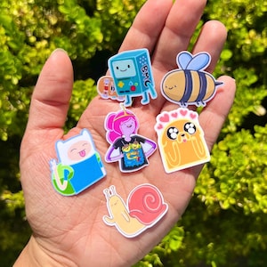 May include: A collection of six Adventure Time character stickers. The stickers feature Finn the Human, Jake the Dog, Princess Bubblegum, BMO, Marceline the Vampire Queen, and a bee. The stickers are all in a cartoon style and are perfect for adding a touch of fun to any project.