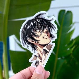 May include: A sticker featuring a close-up of a young man with black hair looking up. He is wearing a brown and white jacket. The sticker is on a white background.