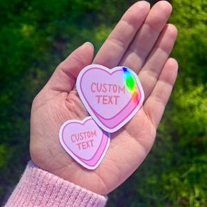 May include: Two pink heart-shaped stickers with the text "CUSTOM TEXT" on each. The stickers have a holographic finish.