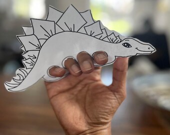 Può includere: Un disegno in bianco e nero di un dinosauro Stegosauro, stampato su carta bianca. Il dinosauro è tenuto da una mano.