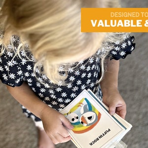 May include: A young girl in a black and white floral dress holds a stack of colorful cards with illustrations of animals and the text "Puffin Rock". The cards are designed to make screen time valuable and enriching.