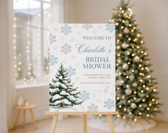 May include: A rectangular sign featuring a white background with blue snowflake illustrations and a snow-covered pine tree. The text reads: WELCOME TO Charlotte's BRIDAL SHOWER DECEMBER 8TH, 20XX GRAND FORKS, ND 70 DAYS UNTIL SHE SAYS i do.