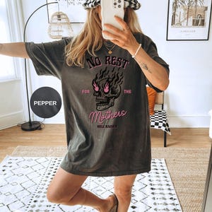May include: A black t-shirt with a graphic of a skull with flames coming out of its eyes. The text "NO REST FOR THE MOTHERS HELL RAISER" is printed on the shirt.
