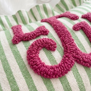 a close-up view of a textured fabric with a pink, crocheted or knitted letter "J" prominently displayed.