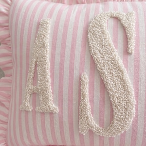 A close-up image of a pink and white striped pillow with the letters 'A' and 'S' embroidered on it.