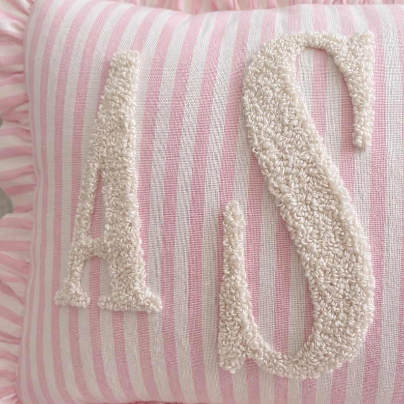 A close-up image of a pink and white striped pillow with the letters 'A' and 'S' embroidered on it.