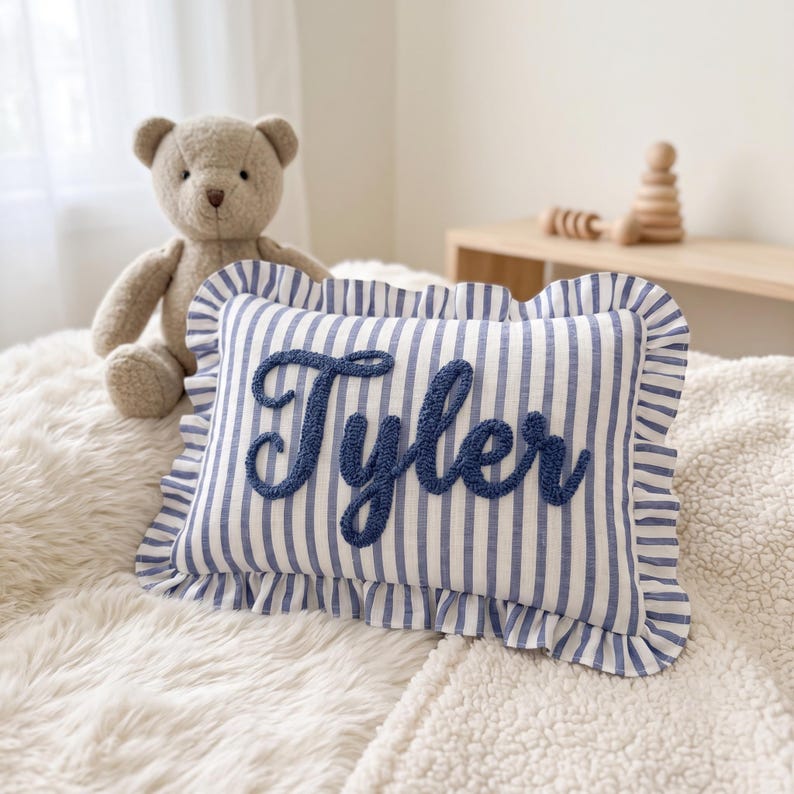 A stuffed teddy bear sits on a bed next to a pillow with the name " Tyler" embroidered on it.