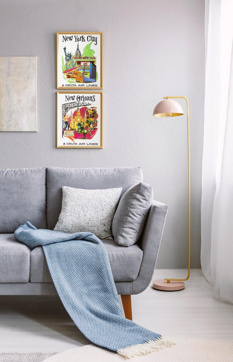 Puede incluir: Un sof&aacute; gris claro con un coj&iacute;n blanco moteado y una manta azul texturizada. Junto al sof&aacute; hay una l&aacute;mpara de pie con estructura de metal dorado, una pantalla en forma de c&uacute;pula rosa p&aacute;lido y una base circular a juego en rosa p&aacute;lido.