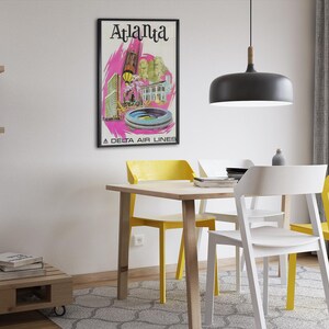 Puede incluir: Un p&oacute;ster de viaje de estilo vintage enmarcado con el texto Atlanta y A Delta Air Lines en la parte inferior. La obra muestra ilustraciones estilizadas de edificios de la ciudad y un estadio en tonos rosa, amarillo y verde sobre fondo blanco.