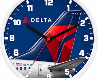 Puede incluir: Un reloj de pared redondo con marco blanco y esfera azul que muestra el estabilizador vertical de un Boeing 737-800 de Delta Airlines. El reloj presenta números blancos del 1 al 12, manecillas negras de hora y minuto, un segundero rojo y el texto Delta y 737-800.
