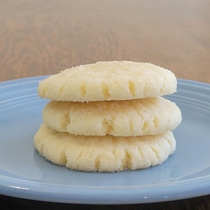 Pode incluir: Três biscoitos de açúcar empilhados em um prato azul claro. Os biscoitos são redondos e têm uma textura ligeiramente áspera.