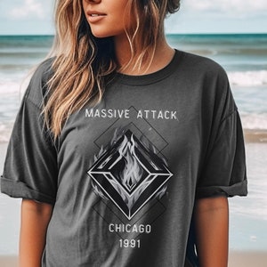May include: A dark gray t-shirt with a graphic design of a stylized flame in a diamond shape. The text "MASSIVE ATTACK" is above the graphic and "CHICAGO 1991" is below the graphic.