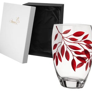 May include: A clear glass vase with a red leaf design. The vase is in a white box with the text "Anna's" on the front.