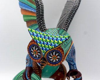 May include: A colorful wooden owl sculpture with outstretched wings, holding a snake in its talons. The owl is painted in shades of blue, green, red, and yellow, with intricate details and patterns.