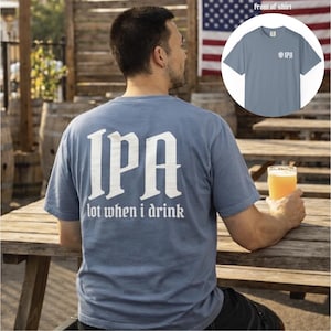 May include: A blue t-shirt with the letters "IPA" in large white gothic font on the back, with the text "lot when I drink" below. The front of the shirt has a small "IPA" logo. The shirt is worn by a person.