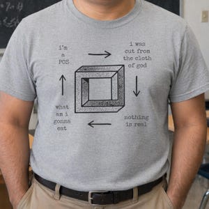 Puede incluir: Una camiseta gris con un gráfico negro de un cubo imposible y texto. El texto incluye frases como "I'm a POS", "I was cut from the cloth of god", "What am I gonna eat" y "Nothing is real".