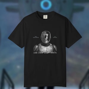 May include: Black t-shirt with a robot graphic, including the text "99% Soap Opera, 1% Murder" and "SEC UNIT 238776431". The robot has a circular eye and armour-like details. The shirt is a crew neck.