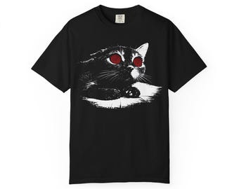 Op de afbeelding: Zwart T-shirt met een zwart-witte illustratie van een kat met rode ogen. De kat ligt met zijn hoofd opzij. De afbeelding is in zwart en wit, met rode ogen.