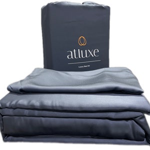 May include: A gray luxury sheet set folded in a stack. The top sheet has the brand name "atluxe" printed on it.