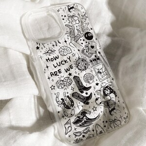 May include: Transparent phone case with a black and white illustrated design. The case features various drawings, including a mermaid, cowboy boots, a disco ball, and the text "HOW LUCKY ARE WE". The case is made of a clear material.