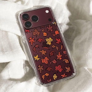 May include: A clear smartphone case featuring a dark maroon background printed with a repeating pattern of autumn leaves in shades of orange, yellow, and red. The case has cutouts for a triple-lens camera system and a flash on the upper left.