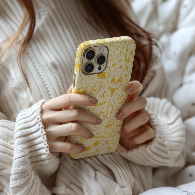 May include: A yellow phone case with a beach-themed design. The case features a variety of illustrations, including flip-flops, sunglasses, and the words "at the beach".
