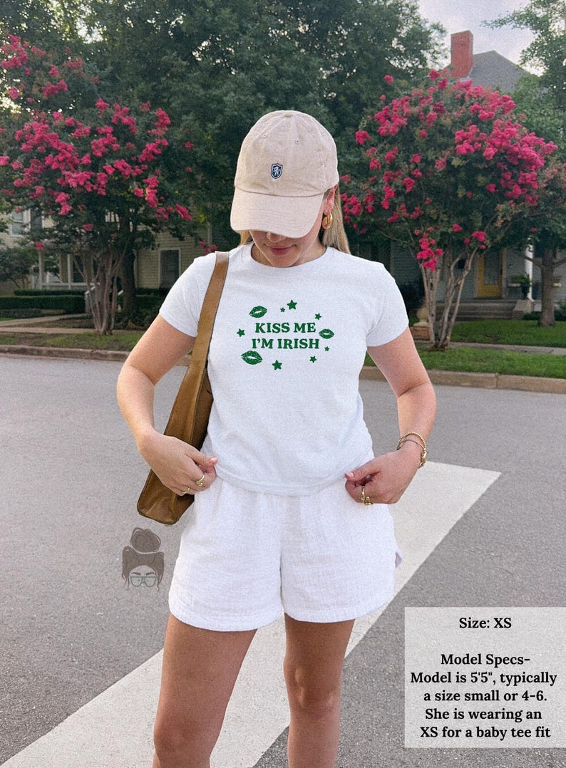 May include: White t-shirt with the text "KISS ME I'M IRISH" in green, paired with white shorts and a beige baseball cap. The image shows a casual outfit, perfect for St. Patrick's Day or any Irish-themed event.