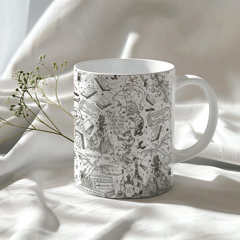 K&ouml;nnte beinhalten: Wei&szlig;e Keramiktasse mit einer Schwarzwei&szlig;illustration von B&uuml;chern, Drachen und anderen Fantasy-Elementen. Der Text auf der Tasse lautet "Es war einmal ein M&auml;dchen, das es liebte zu lesen" und "Fantasy Book Club".