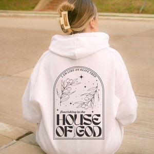 Puede incluir: Sudadera con capucha blanca con un dise&ntilde;o gr&aacute;fico negro que representa un olivo con el texto "I am like an olive tree flourishing in the HOUSE OF GOD".