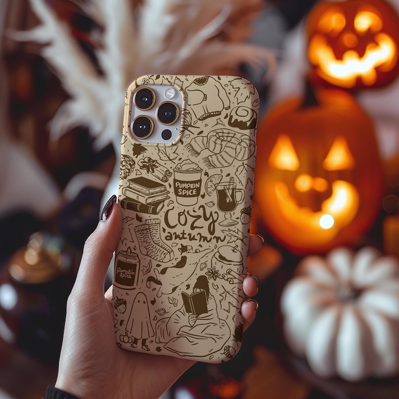 May include: A tan phone case with a brown autumn-themed design. The case features illustrations of books, a coffee cup, a ghost, and the words "Cozy Autumn" and "Pumpkin Spice". The case is designed for a smartphone.