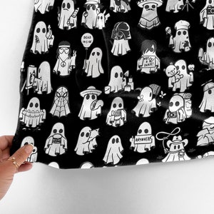 May include: Black fabric with a white repeating pattern of ghosts in various poses and with different accessories. The ghosts are wearing hats, holding cameras, and carrying signs with text like "Dead Inside" and "Anywhere".