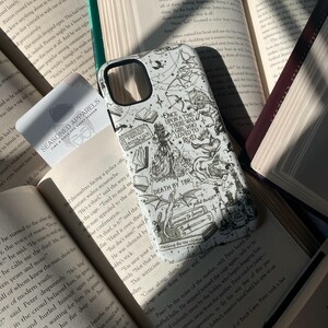 May include: A white smartphone case featuring black line art illustrations of fantasy elements including a dragon, a mermaid, books, and text that reads Once Upon A Time There Was A Girl Who Loved To Read, Death By TBR, and Enemies To Lovers.